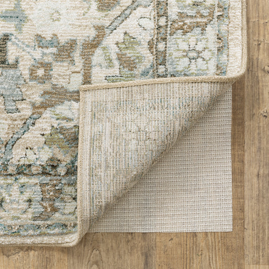 A patterned beige-blue rug corner is folded up, revealing its woven underside and a non-slip rug pad beneath, resting on a light wood floor.