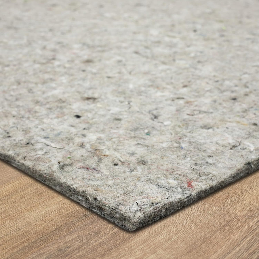 Rectangular gray recycled felt pad lies flat on a wooden floor, showing a close-up of its fibrous, speckled surface and a slightly raised corner.