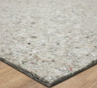 A rectangular gray pad  lies flat, displaying a mottled, fibrous surface and a rounded corner resting on a light wooden floor.