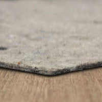 Gray felt rug pad lies flat on a wood surface; its frayed fibers and lint peek along the beveled edge in a shallow, close-up, blurred background.