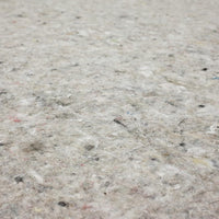 Gray fibrous rug padding lies flat, displaying mottled fibers and small colored flecks across a close-up textile surface.

