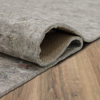 Gray felt rug padding folded back to reveal a textured beige backing, resting on a light wood-grain floor.