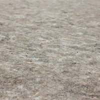 A mottled gray-brown rug pad lies flat, its felt-like texture and small fibers visible in a shallow-depth, close-up view filling the frame with no other objects.