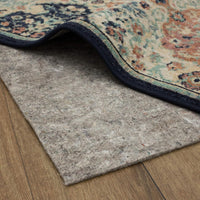 A patterned area rug peels up at one corner, revealing a gray felt rug pad beneath; ornate teal, rust, and cream design with dark blue binding sits atop wood flooring.