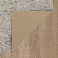 Corner of a beige carpet pad folded back, revealing gray felt padding beneath and light-brown wood-grain flooring underneath in a close-up top-down view.