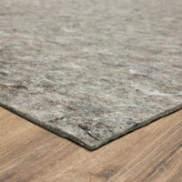 Gray recycled-fiber felt rug pad lies flat across a wooden floor, its textured corner in the foreground and the mottled surface fading toward the background.